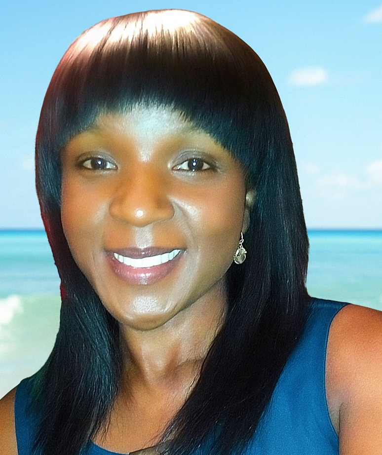 A woman with dark hair smiling, wearing earrings, and a blue top, with a beach and ocean in the background.