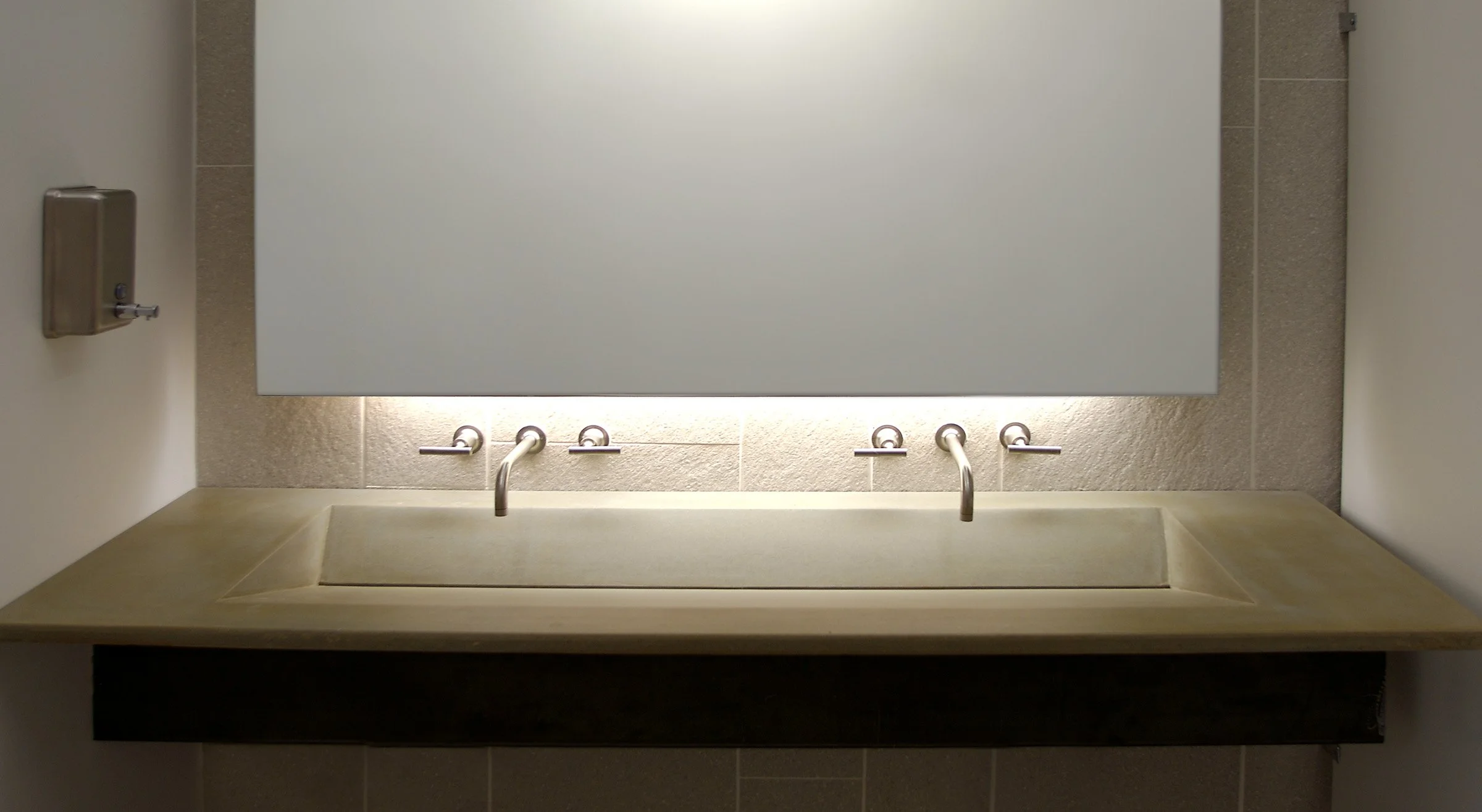 Artisan concrete ramp sink with dual faucets and unique tea-stain surface treatment.