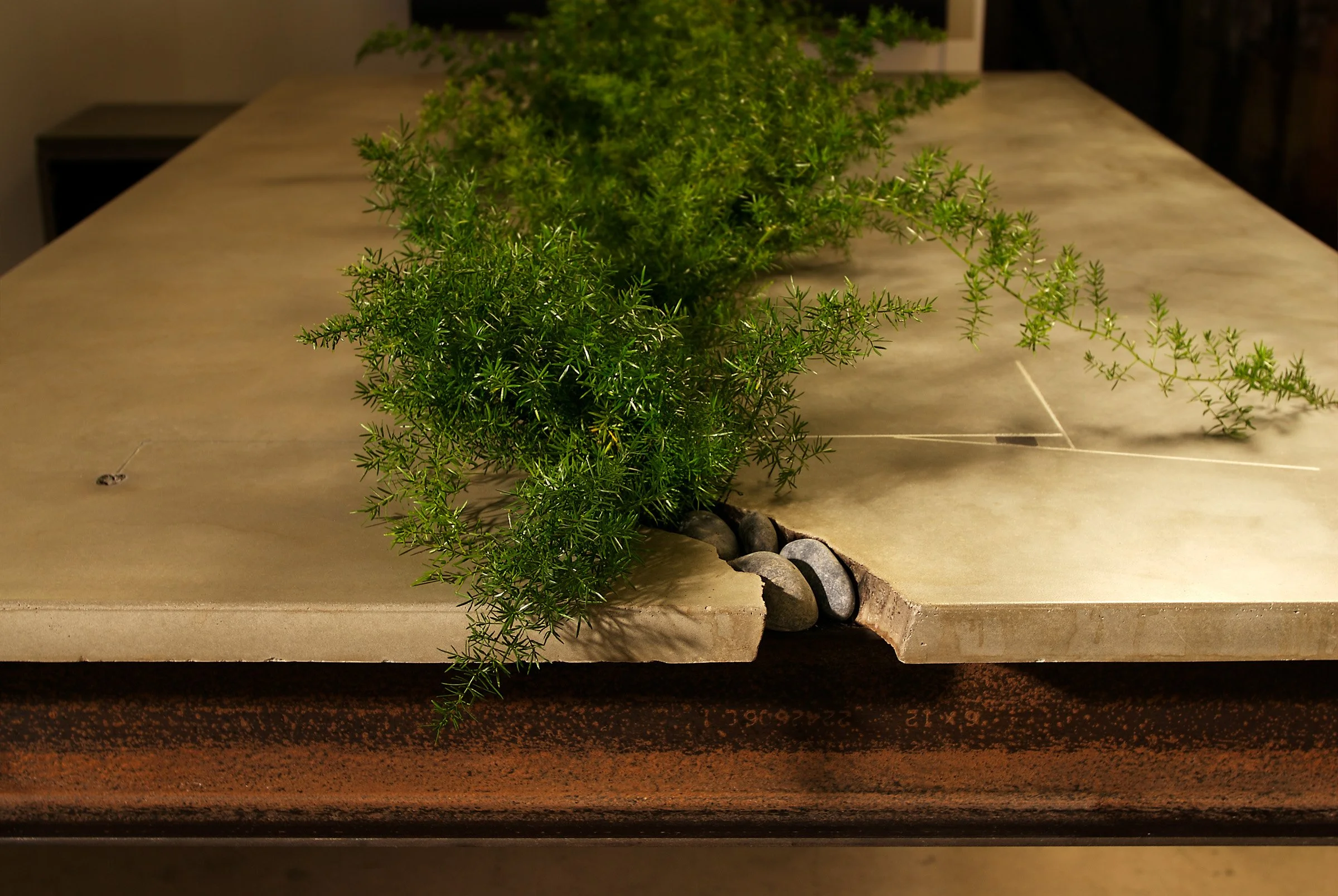 Groundbreaking cracked concrete conference table with central grow tray. Handcrafted GFRC in clay with fossils, meteorite inlays, and steel I-beam base.