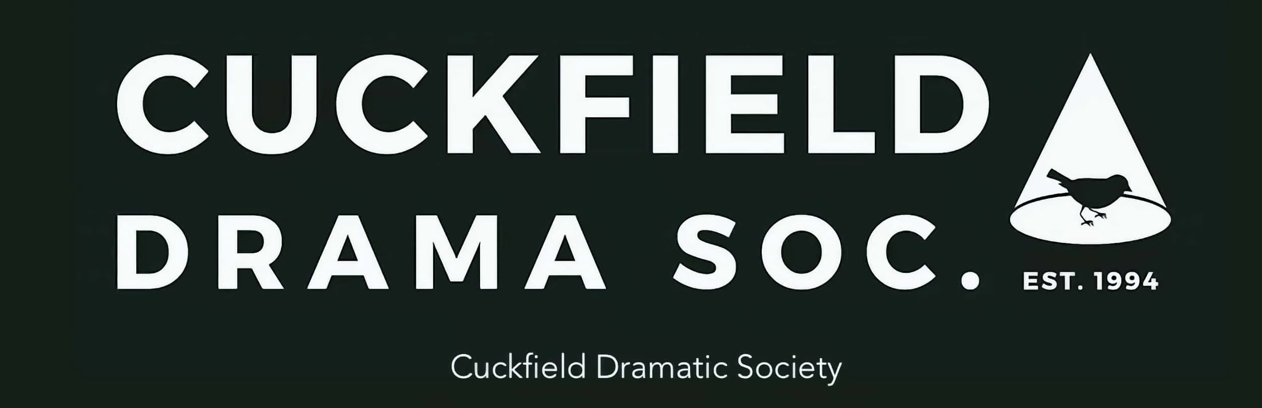 Man in a bright yellow shirt and dark pants playing golf, swinging a club on a lush green golf course with trees and hills in the background under a partly cloudy sky.