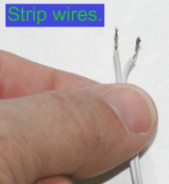 Close-up of a person's finger holding two white stripped wires with exposed metal ends.