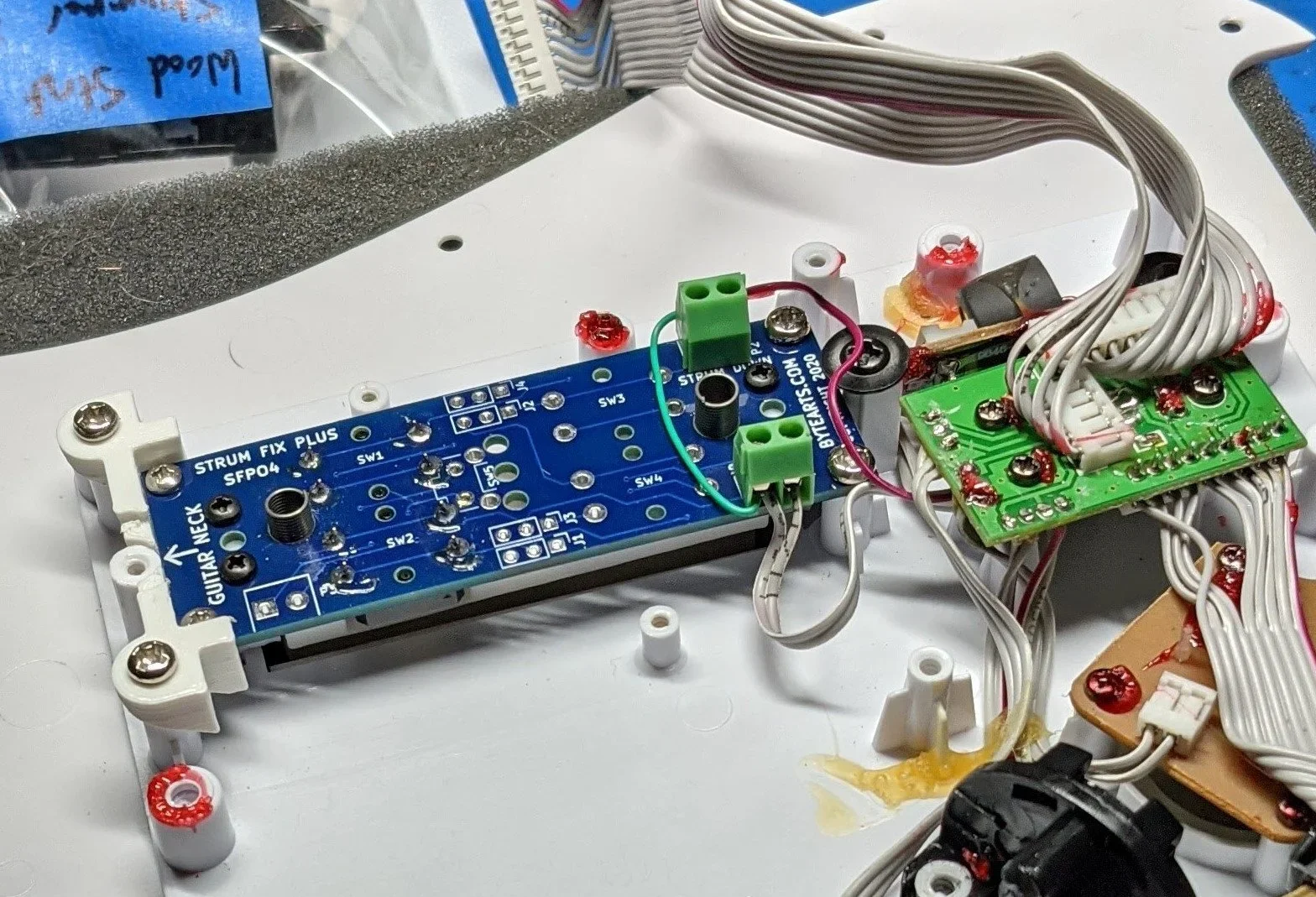 Close-up of disassembled electronic guitar effects pedal with circuit boards, wires, and components on a white surface.