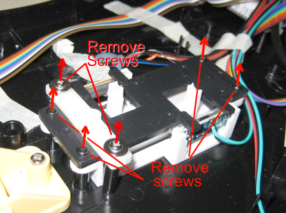 Close-up of electronic device with red arrows pointing to screws, indicating to remove screws in an electronic assembly with wires and plastic components.