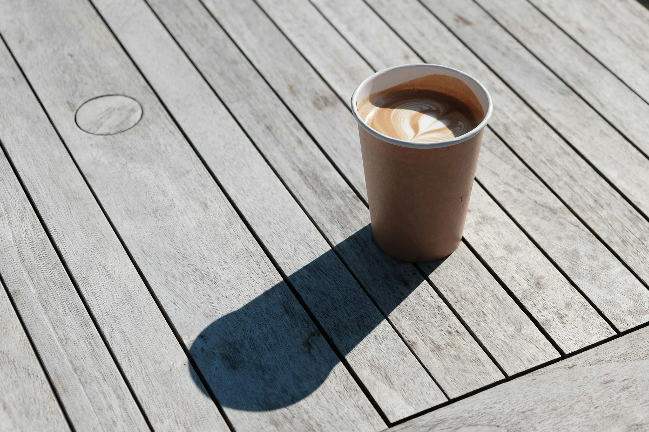 A paper cup of coffee with latte art on a wooden outdoor table at an event in Omaha, NE hosted by Ahamo Coffee Co.