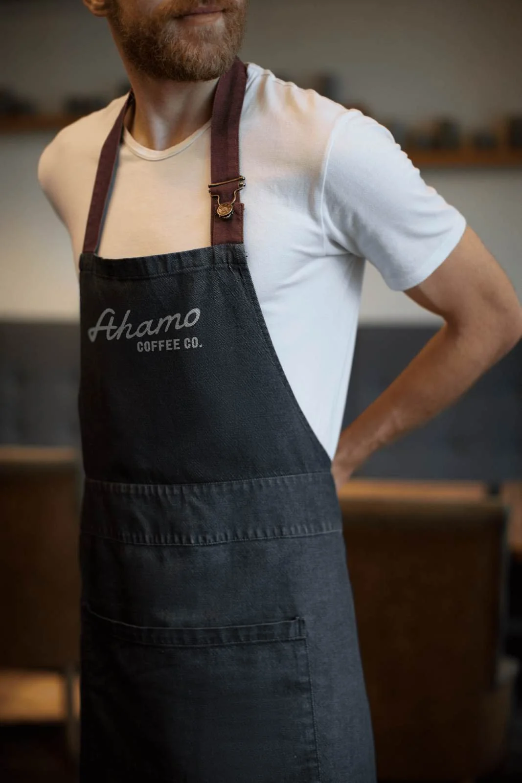Close-up of a man wearing a white t-shirt and a black apron with the logo 'Ahamo Coffee Co.' at an event in Omaha, NE.