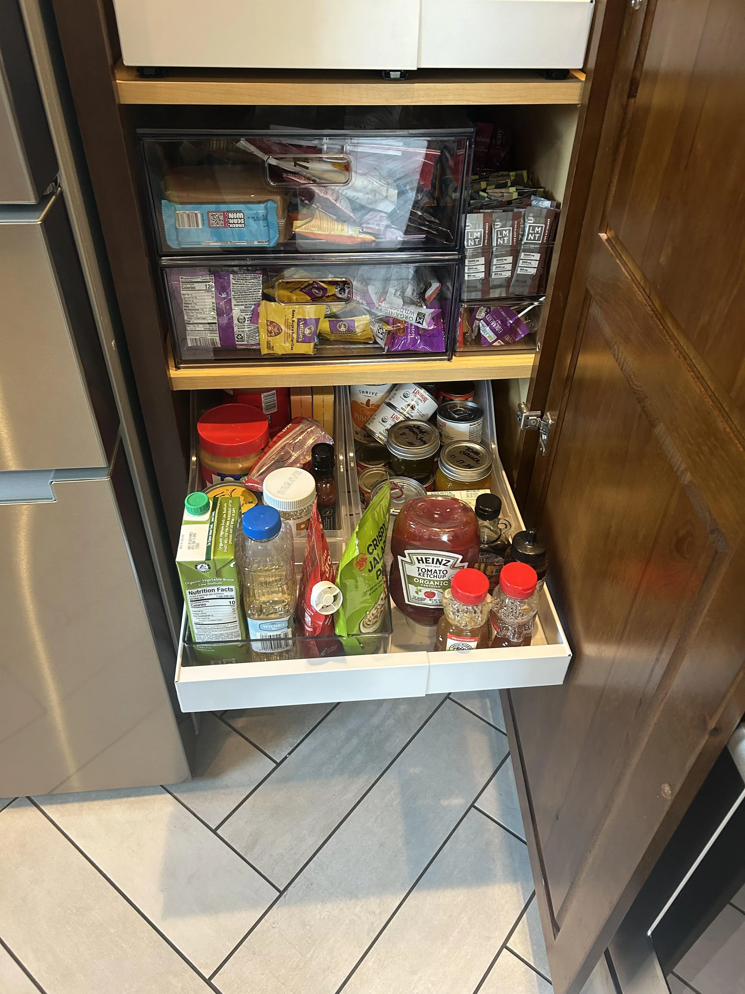 A kitchen drawer open to reveal various condiments, canned goods, snack packs, and other food items stored inside.