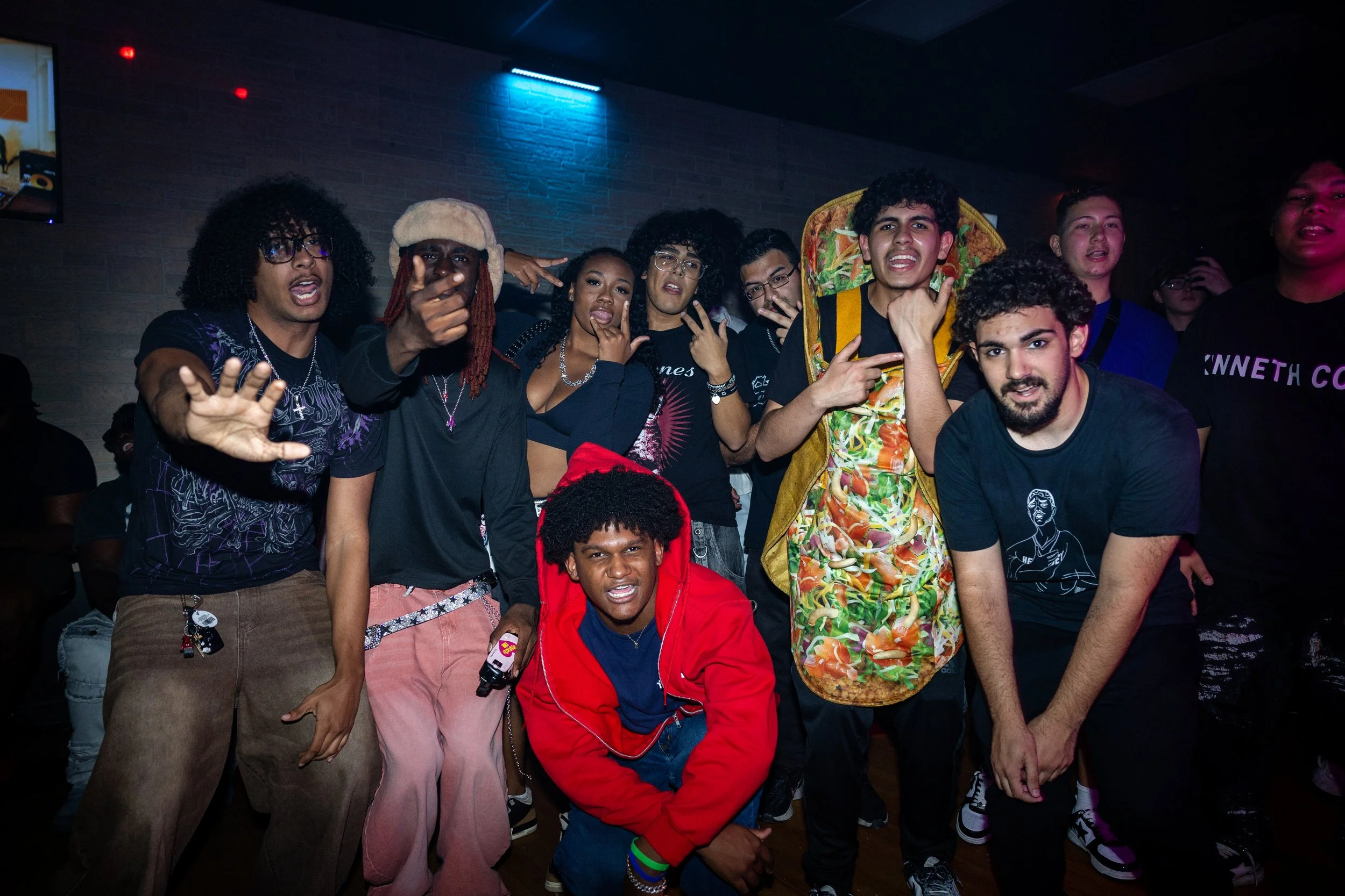 Group of diverse young people posing and making gestures at a party indoors with blue lighting.