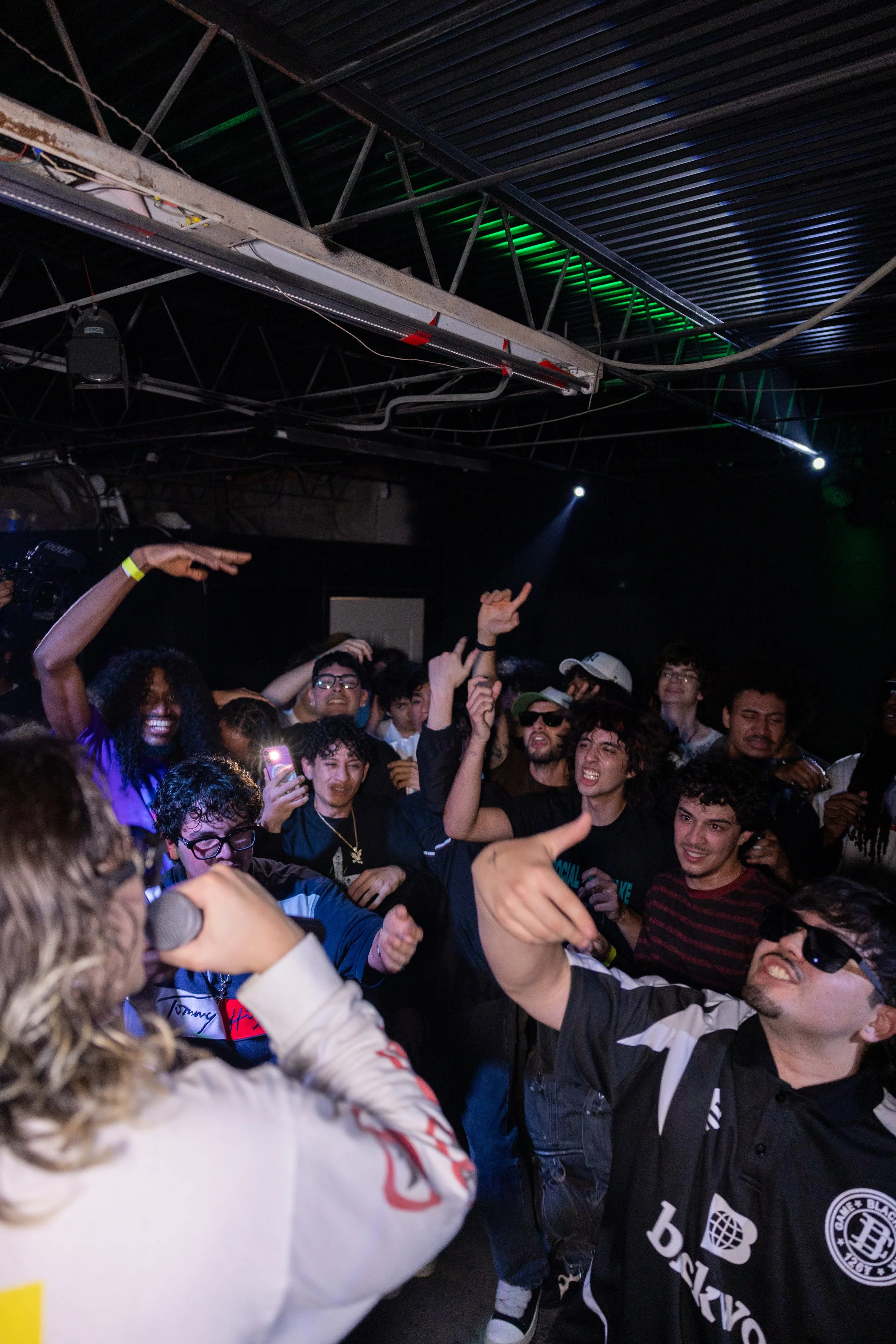 A group of young people at a concert or party, dancing and enjoying themselves in a dimly lit venue with colorful lighting.