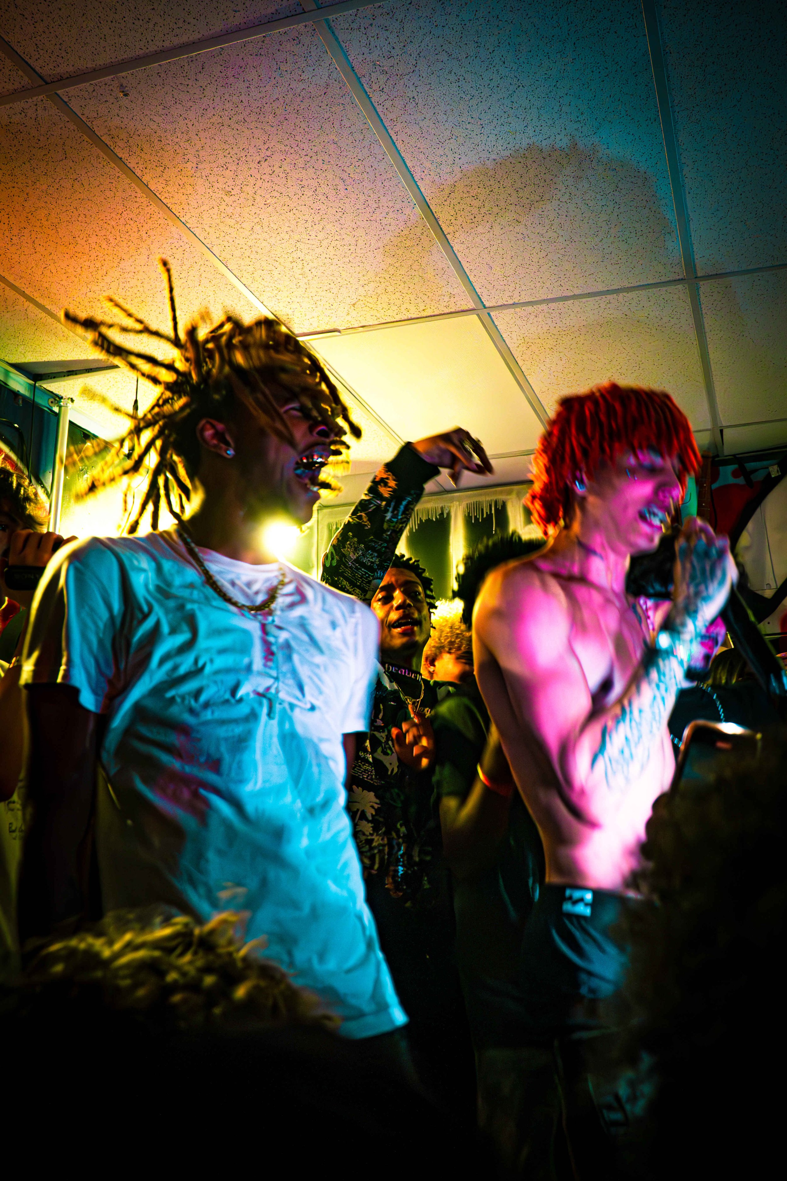People singing and enjoying a live performance at an indoor music event, with colorful lighting illuminating the scene.