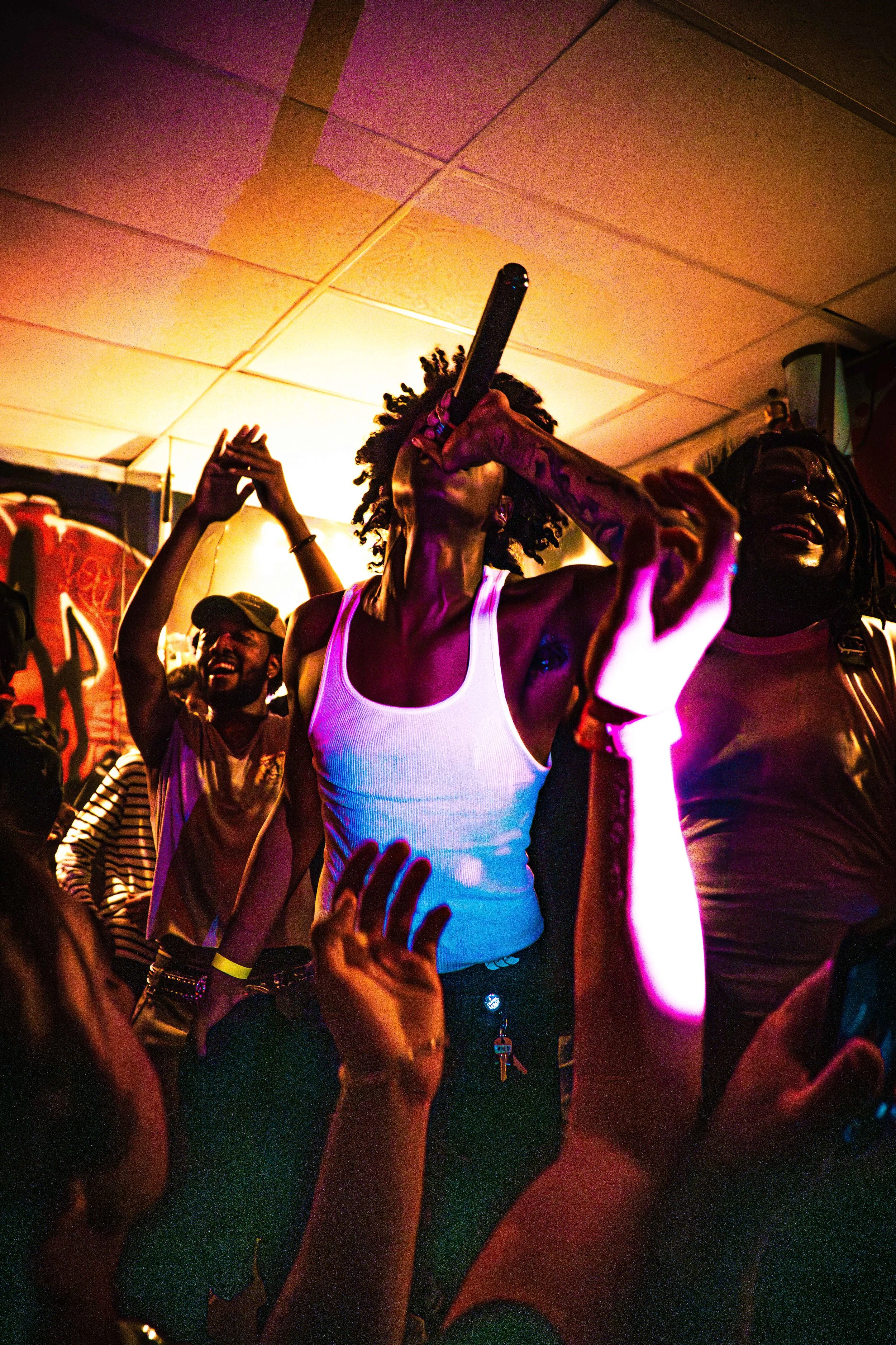 A person singing into a microphone at a lively concert or party, surrounded by others enjoying the music and dancing.