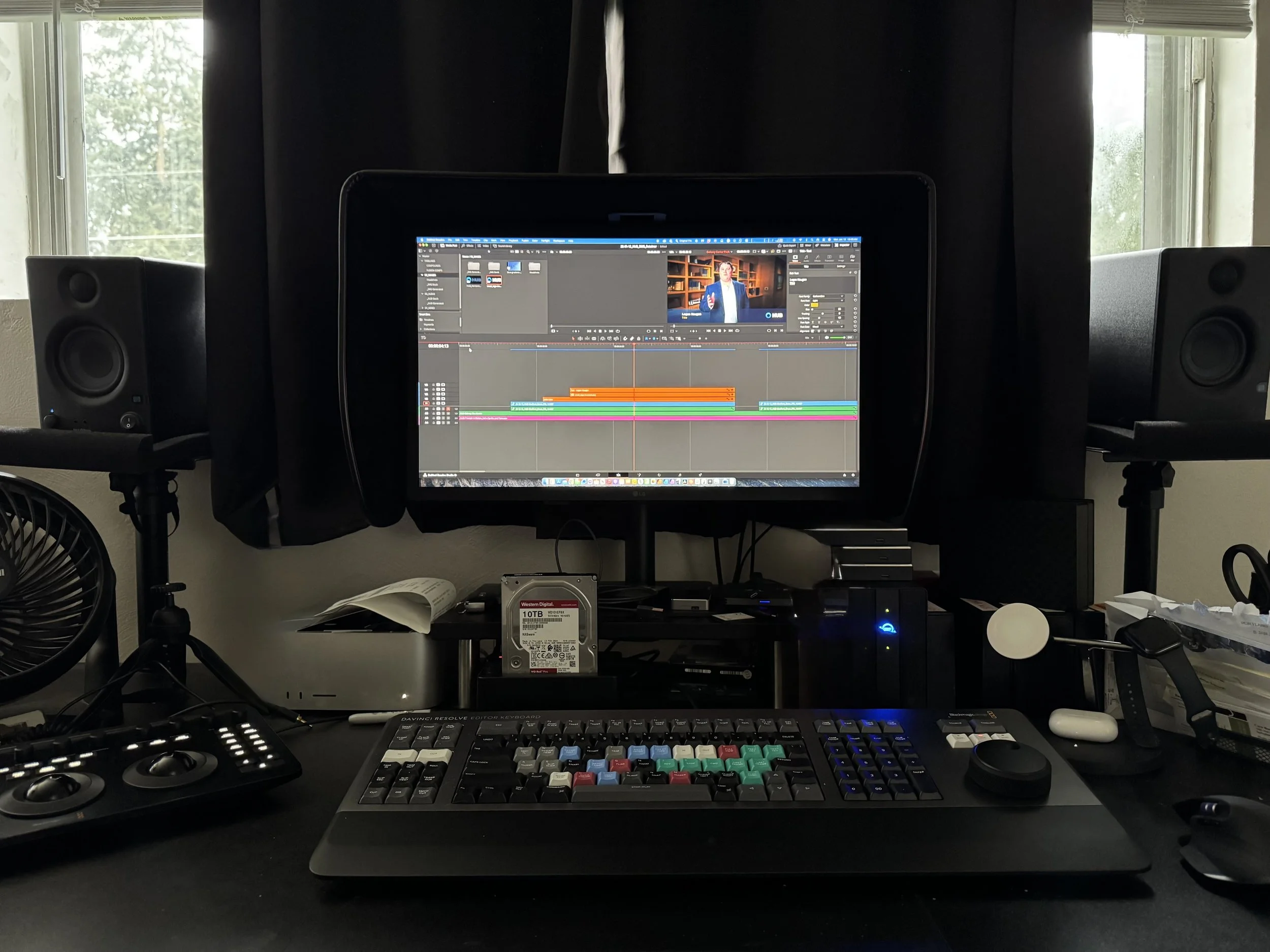 Computer desk with a monitor displaying video editing software, a keyboard, mouse, speakers, and various accessories.