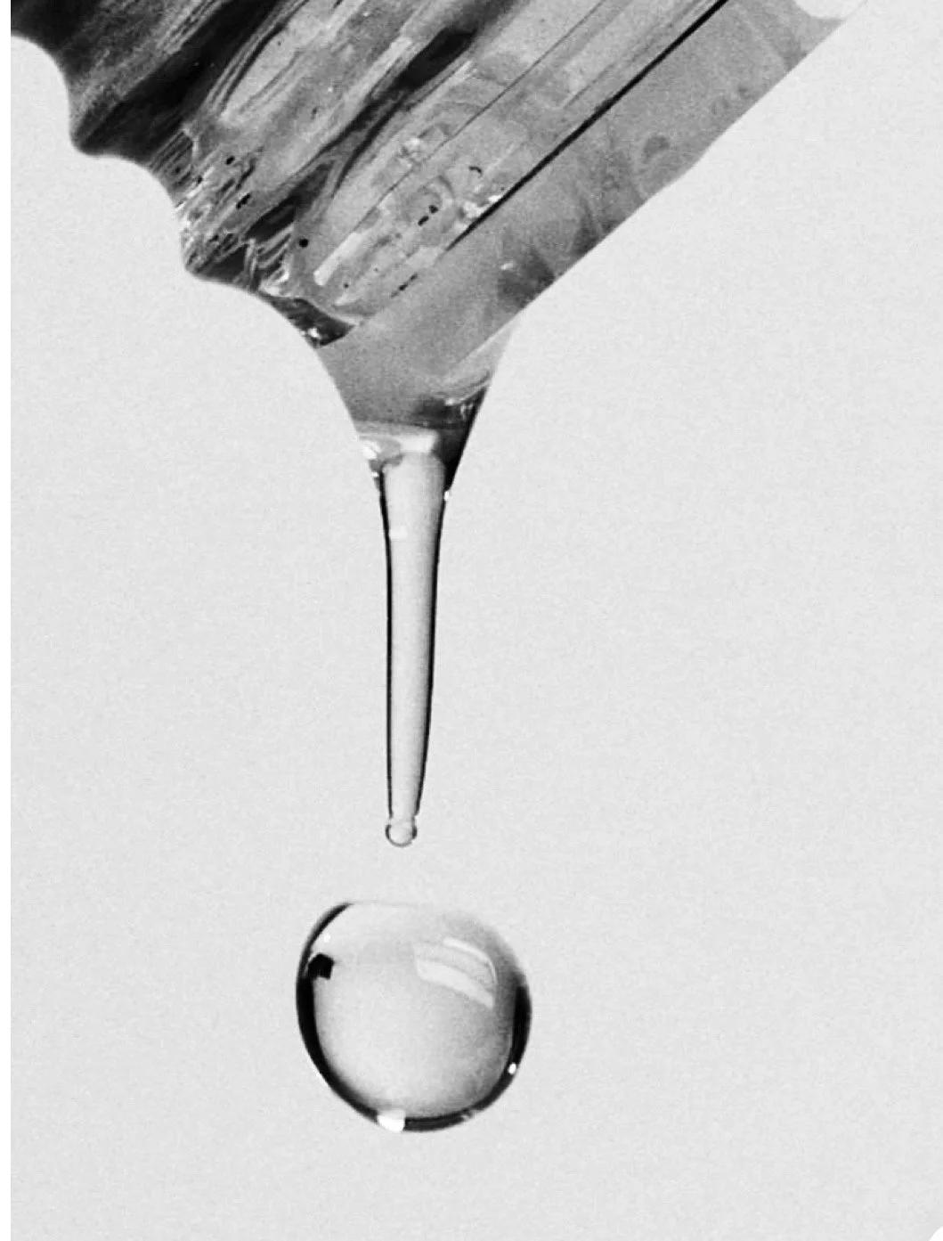 Close-up of a glass dropper releasing a single droplet of liquid onto a reflective surface.