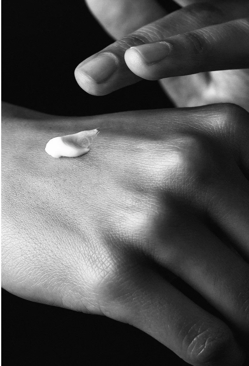 A person applying lotion or cream to the back of their hand in black and white.