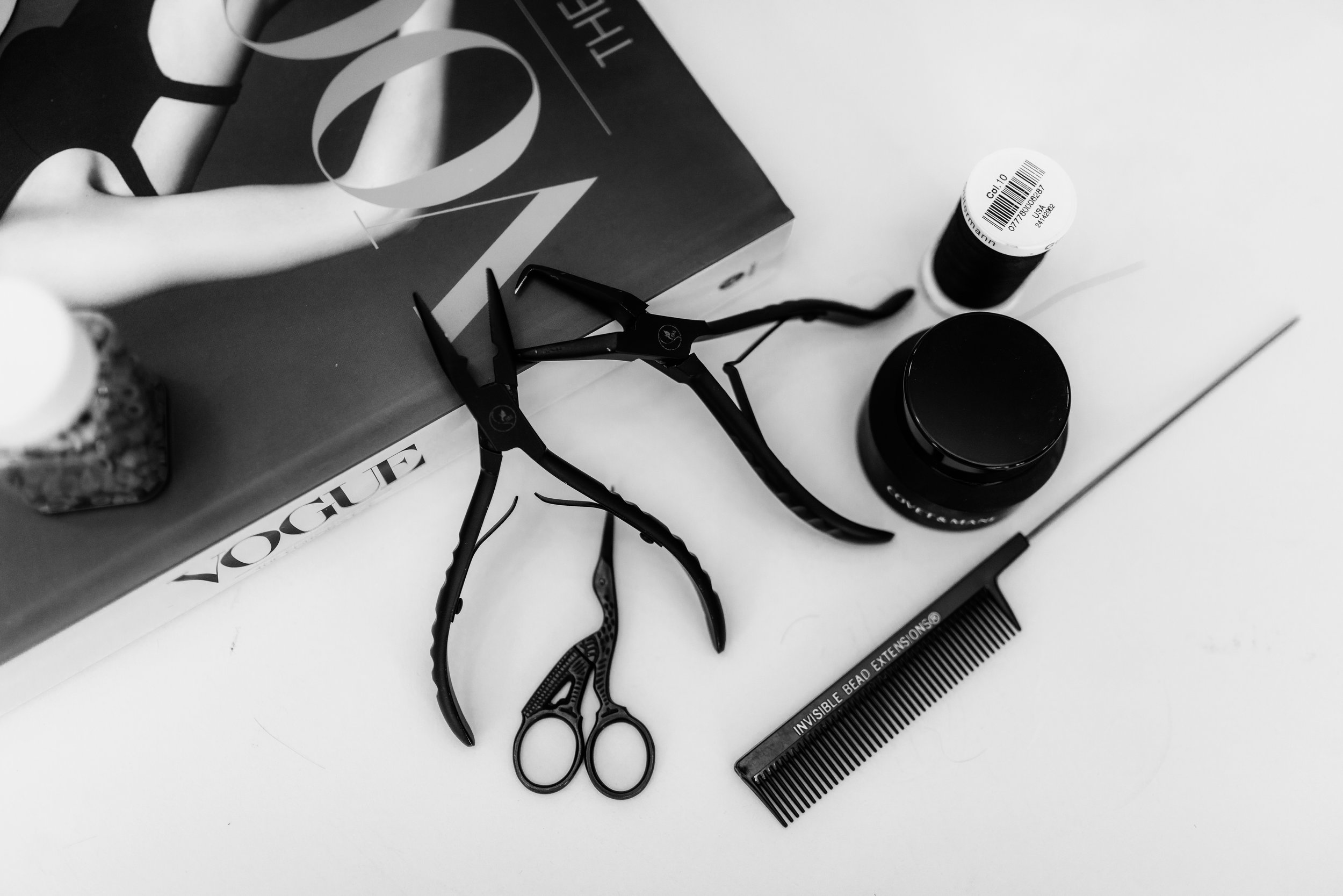 A collection of beauty and grooming tools on a white surface, including black cuticle nippers, a black comb with