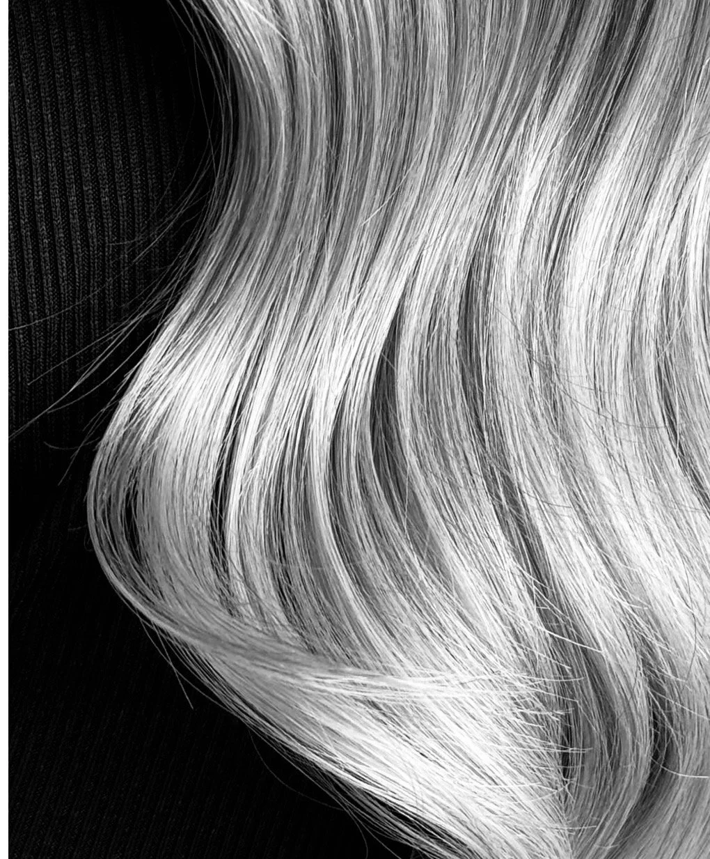 Close-up of silver-blonde hair with soft, flowing waves against a dark background.