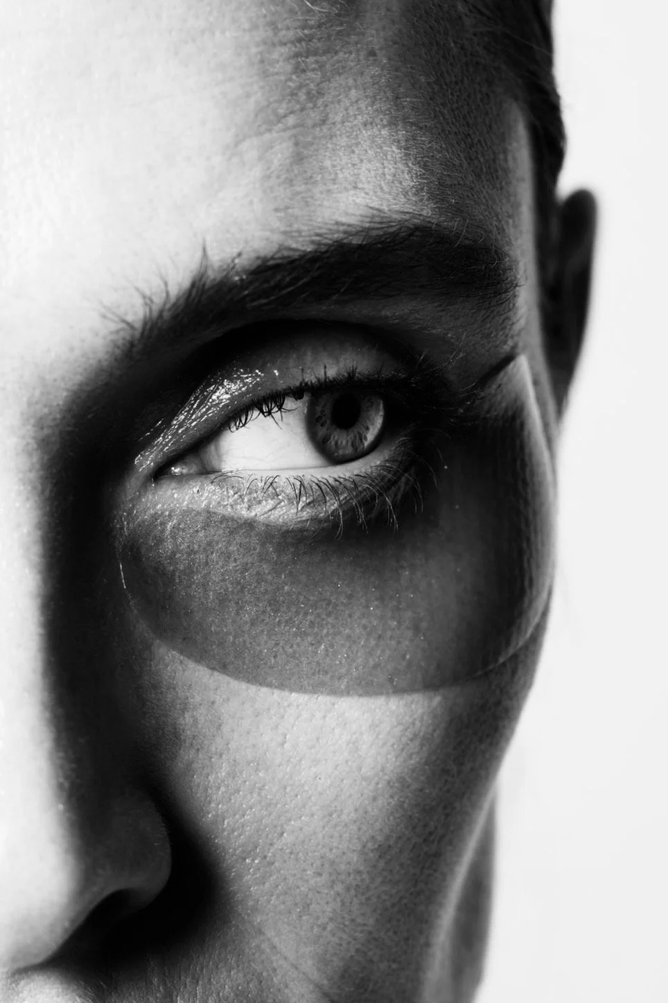 Close-up black and white photograph of a person's eye with detailed eyelashes and eyebrow