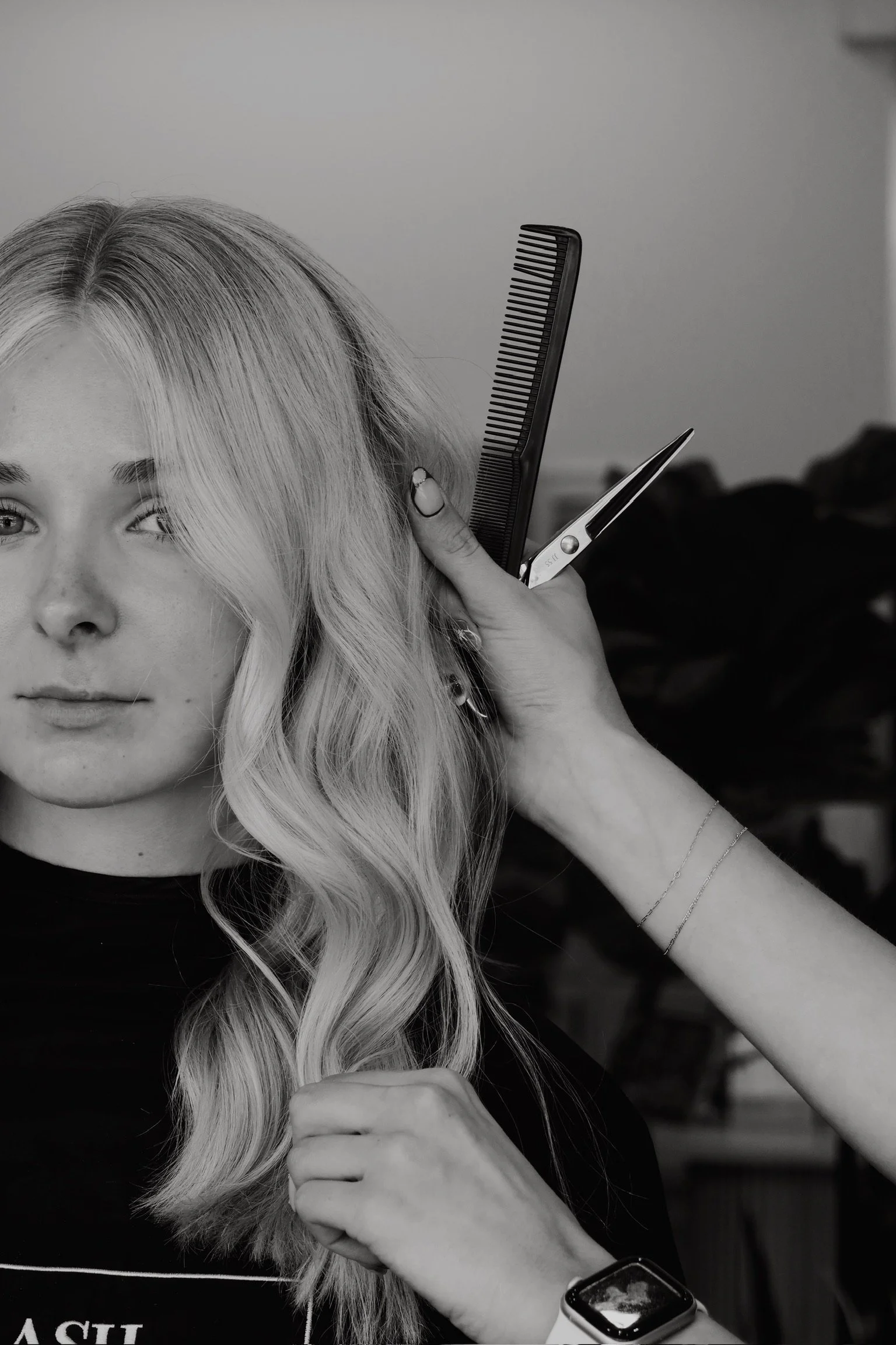 A woman getting her hair styled with a comb and scissors in a salon, black and white photo.