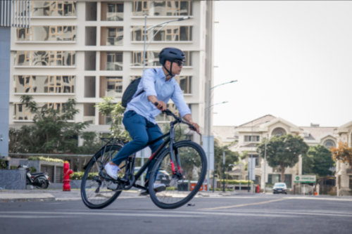 Person riding a bicycle on an urban street in daytime, wearing a helmet and blue clothing.