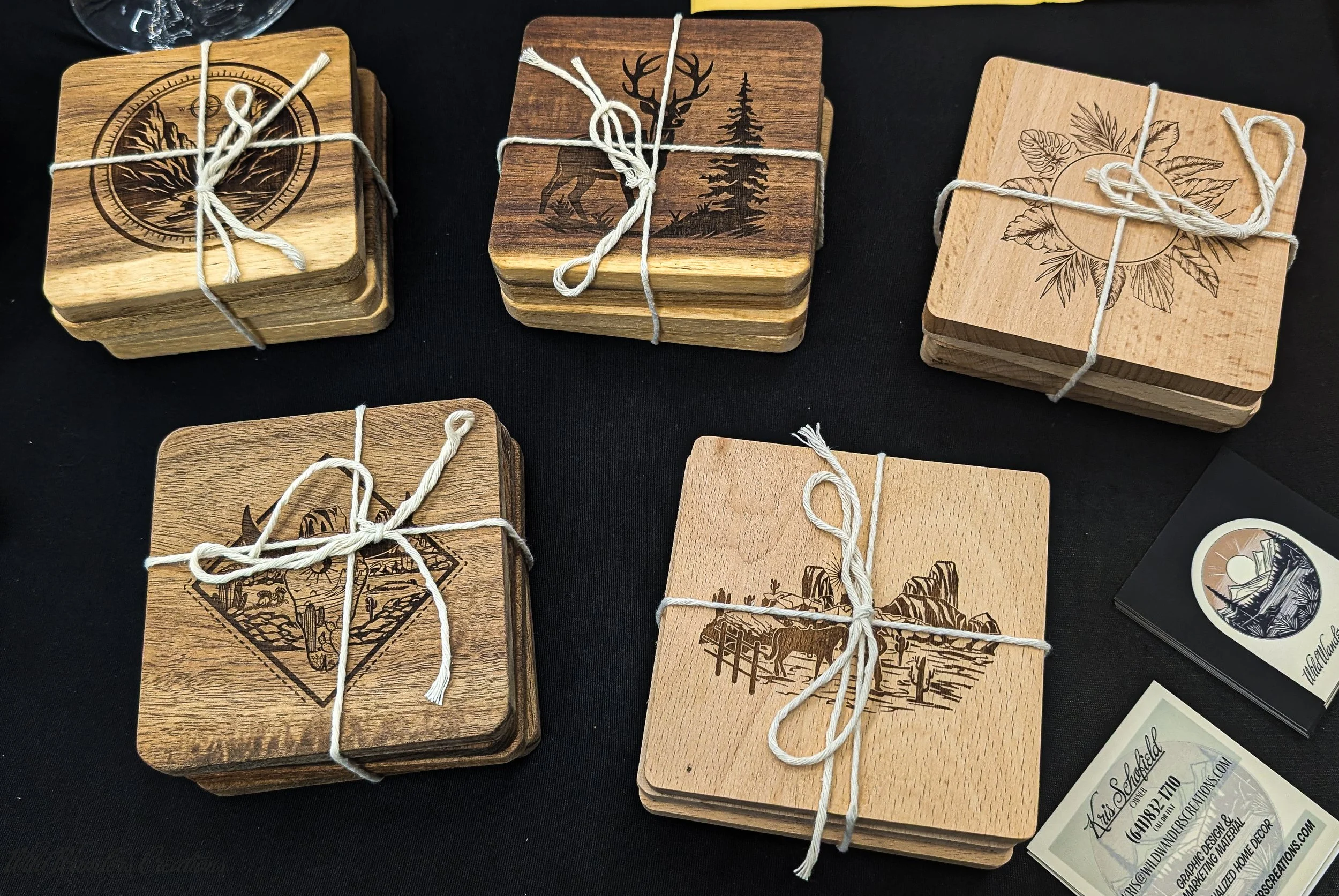 Multiple wooden coasters with engraved nature-themed images, tied with white string, displayed on a black surface.