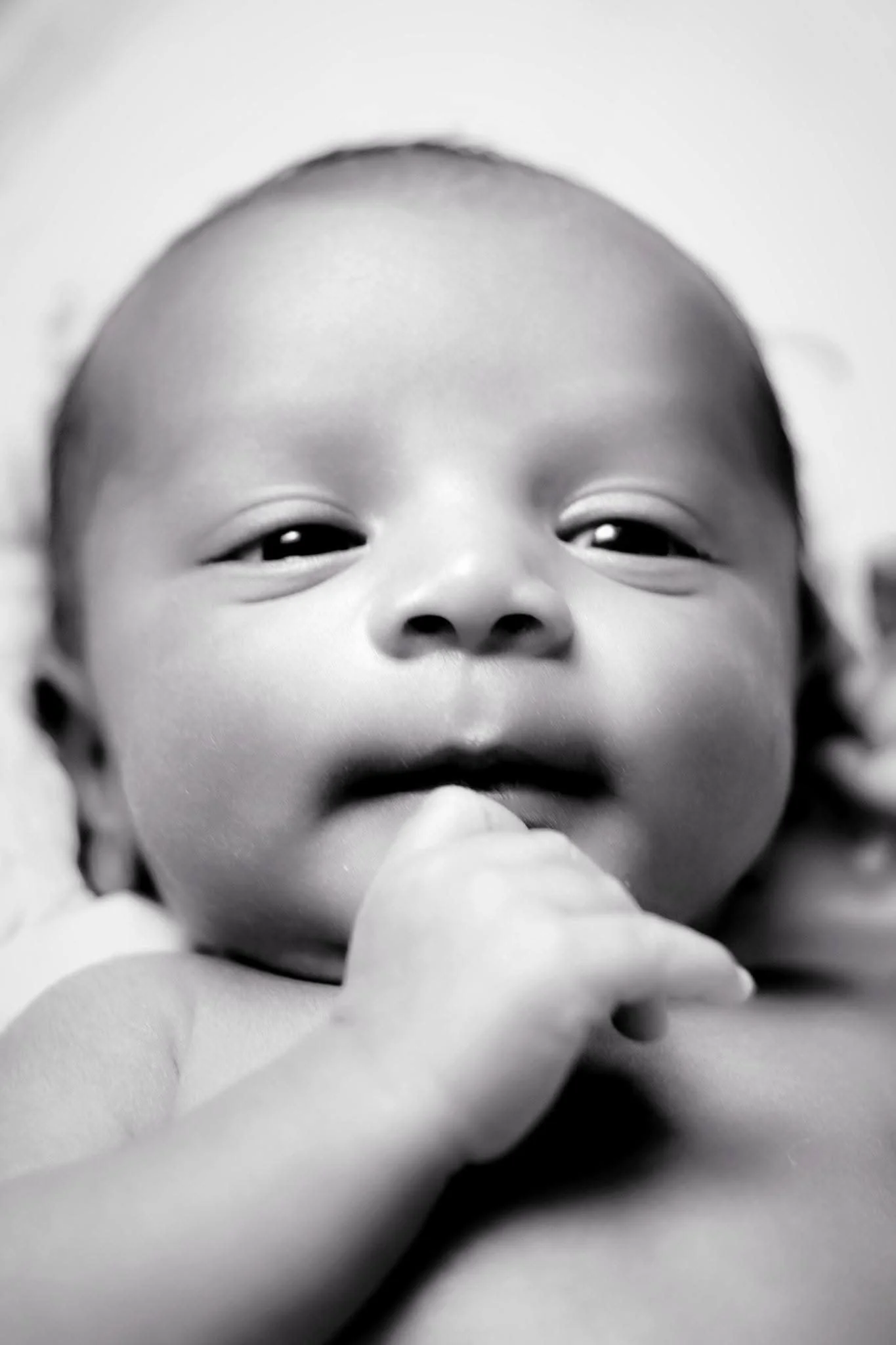 Close-up black and white photo of an infant with a finger near their mouth.