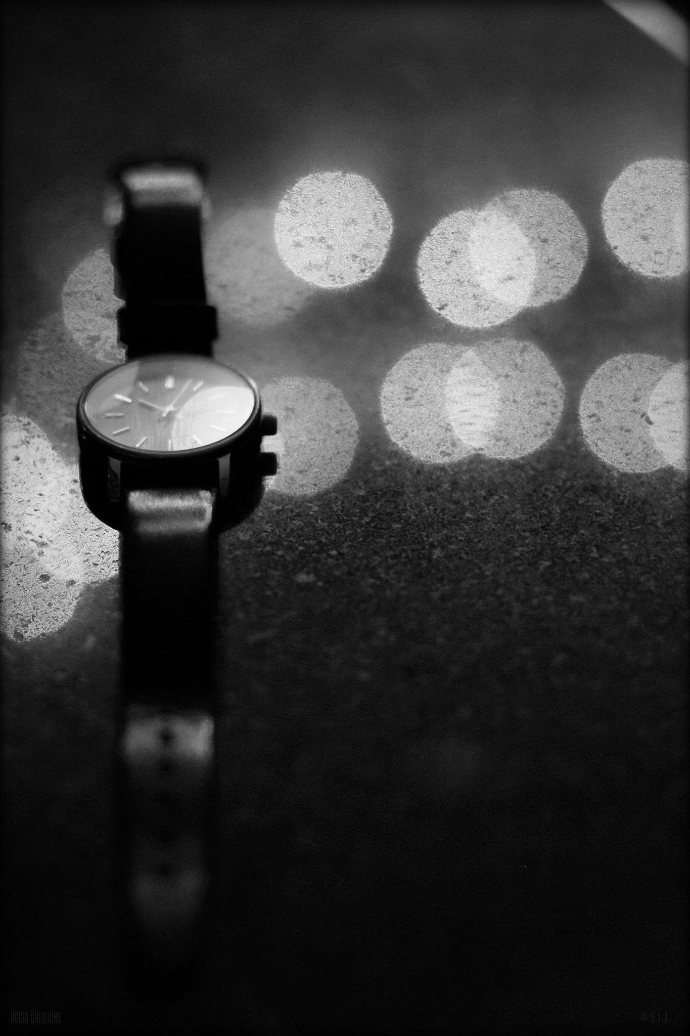 A wristwatch with a leather strap placed on a textured surface with blurred circular light reflections in the background.