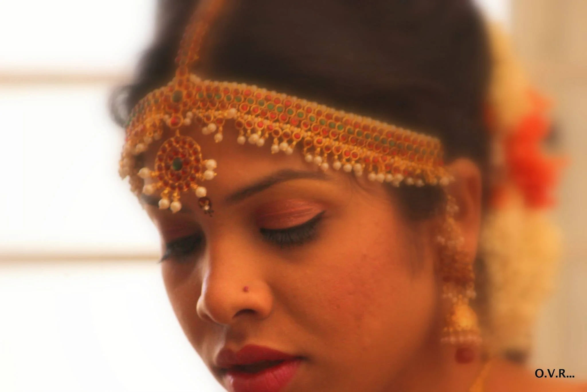 Close-up of a young woman with traditional jewelry and makeup, wearing a decorated headpiece, with her eyes closed.