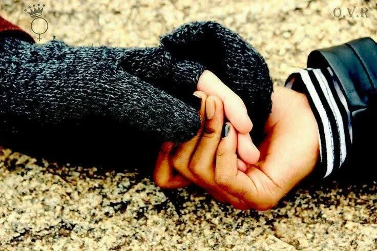 Two people holding hands, one with a darker skin tone wearing a gray sweater and the other with a lighter skin tone wearing a striped sleeve.