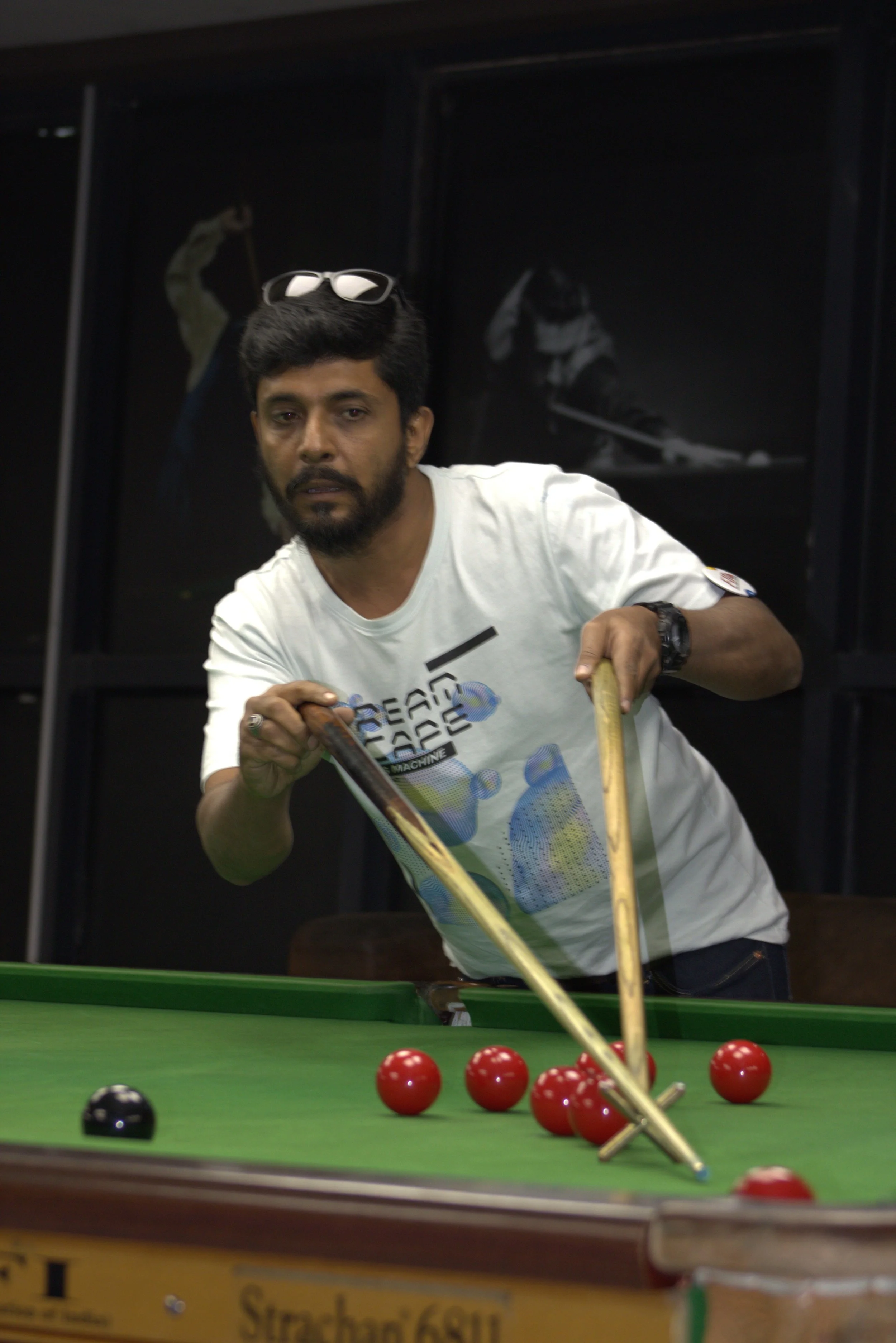 A man playing billiards, aiming to hit red balls on a green felt pool table.