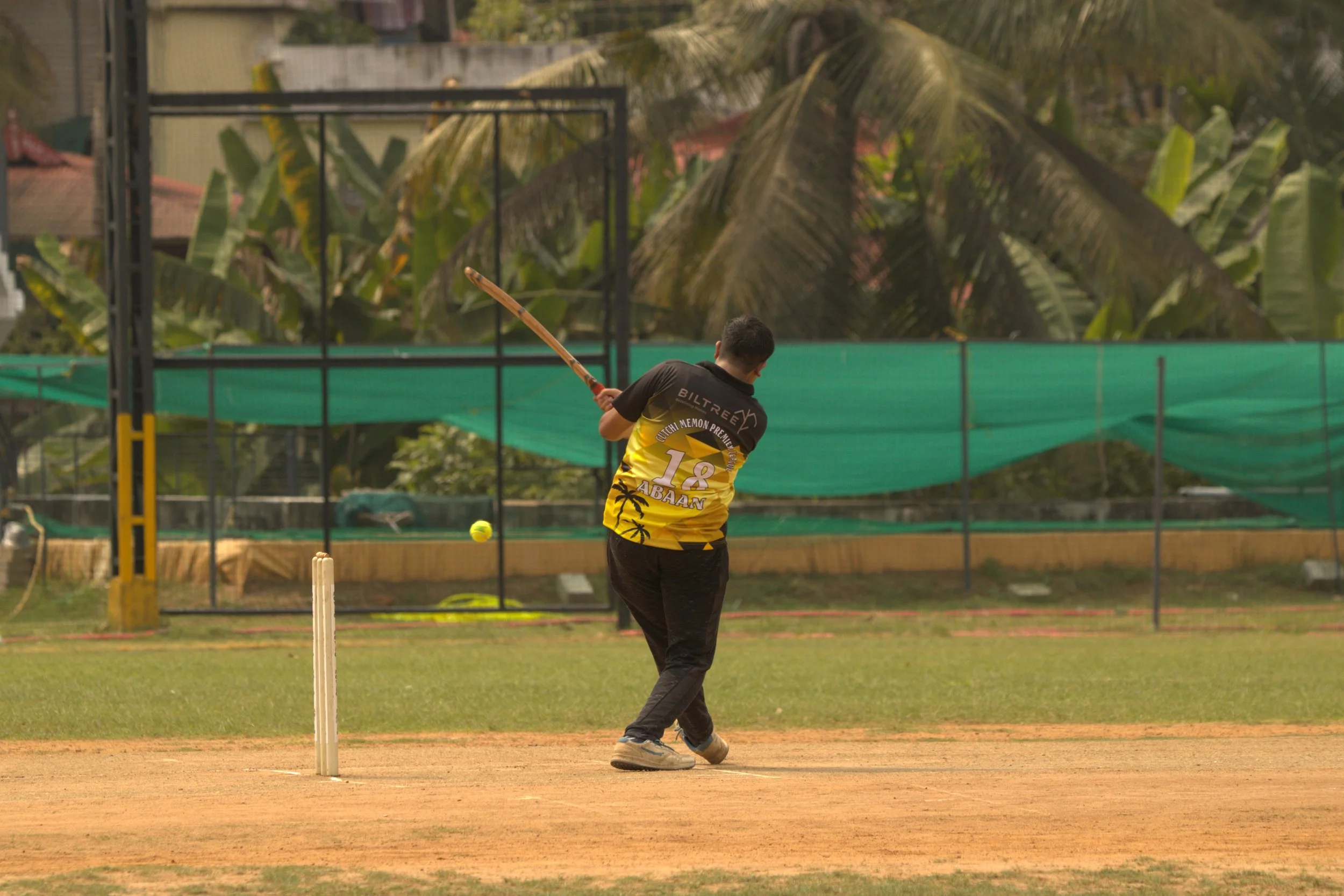 A person playing cricket, swinging a bat on a cricket field.