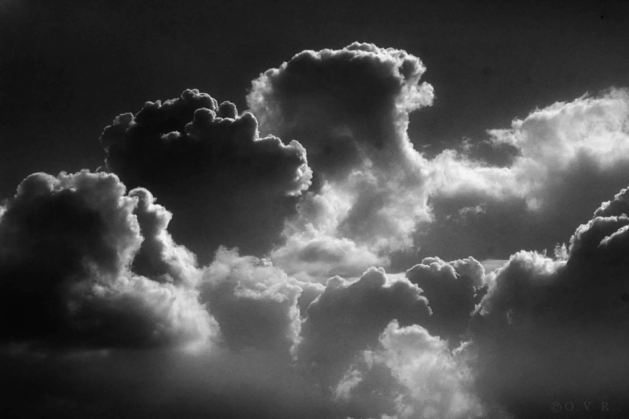 Black and white photograph of clouds in the sky with sunlight illuminating their edges.