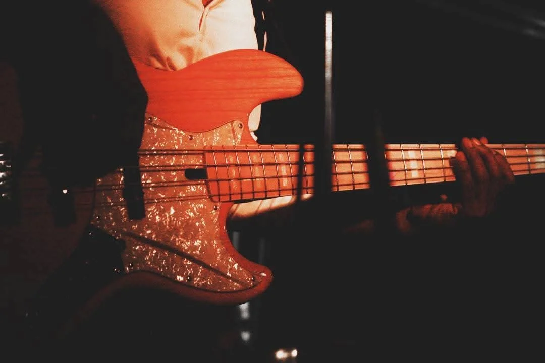 A person playing a red electric bass guitar in a dark setting.