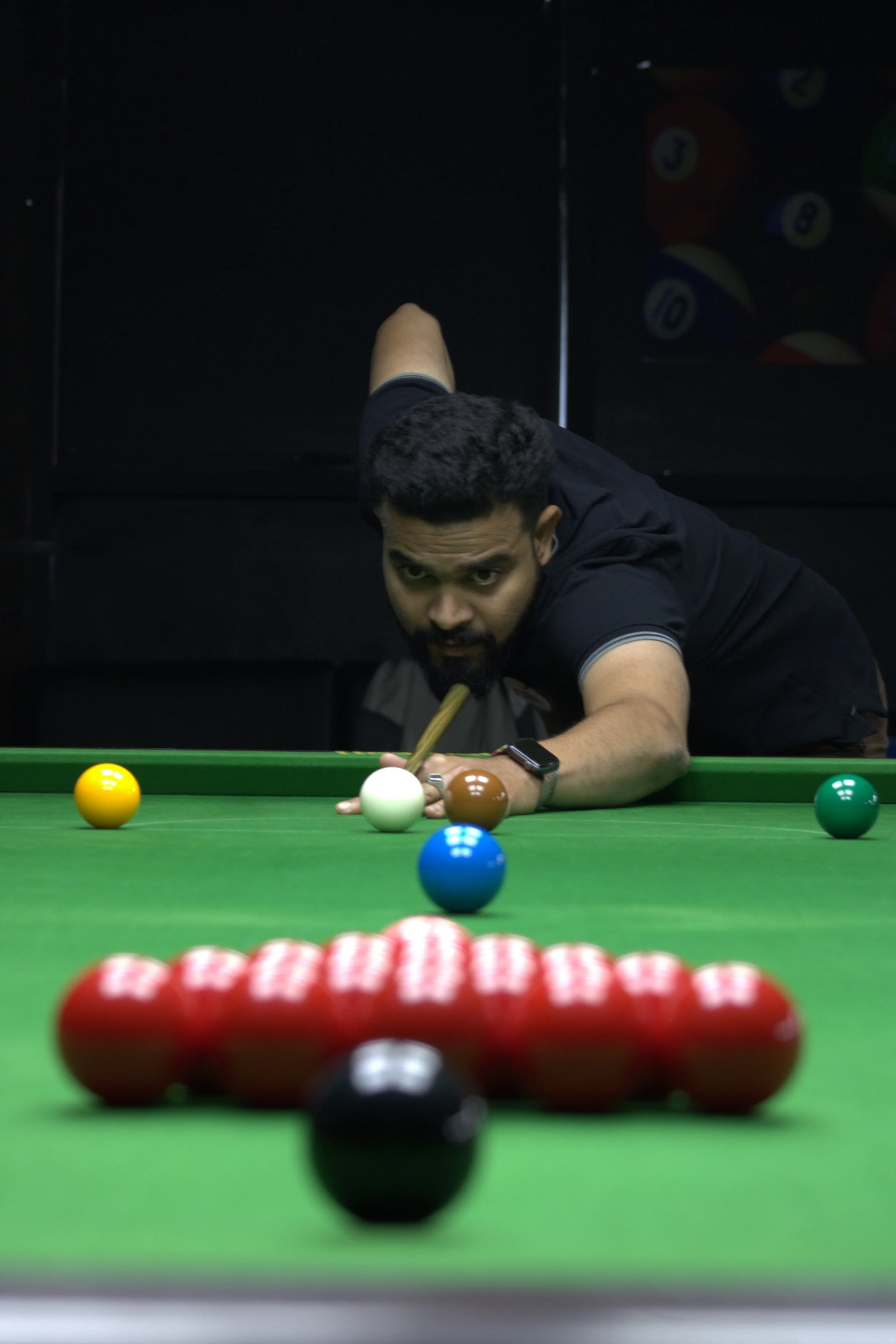 A man playing pool, aiming for a shot on a green billiards table with colorful balls lined up.