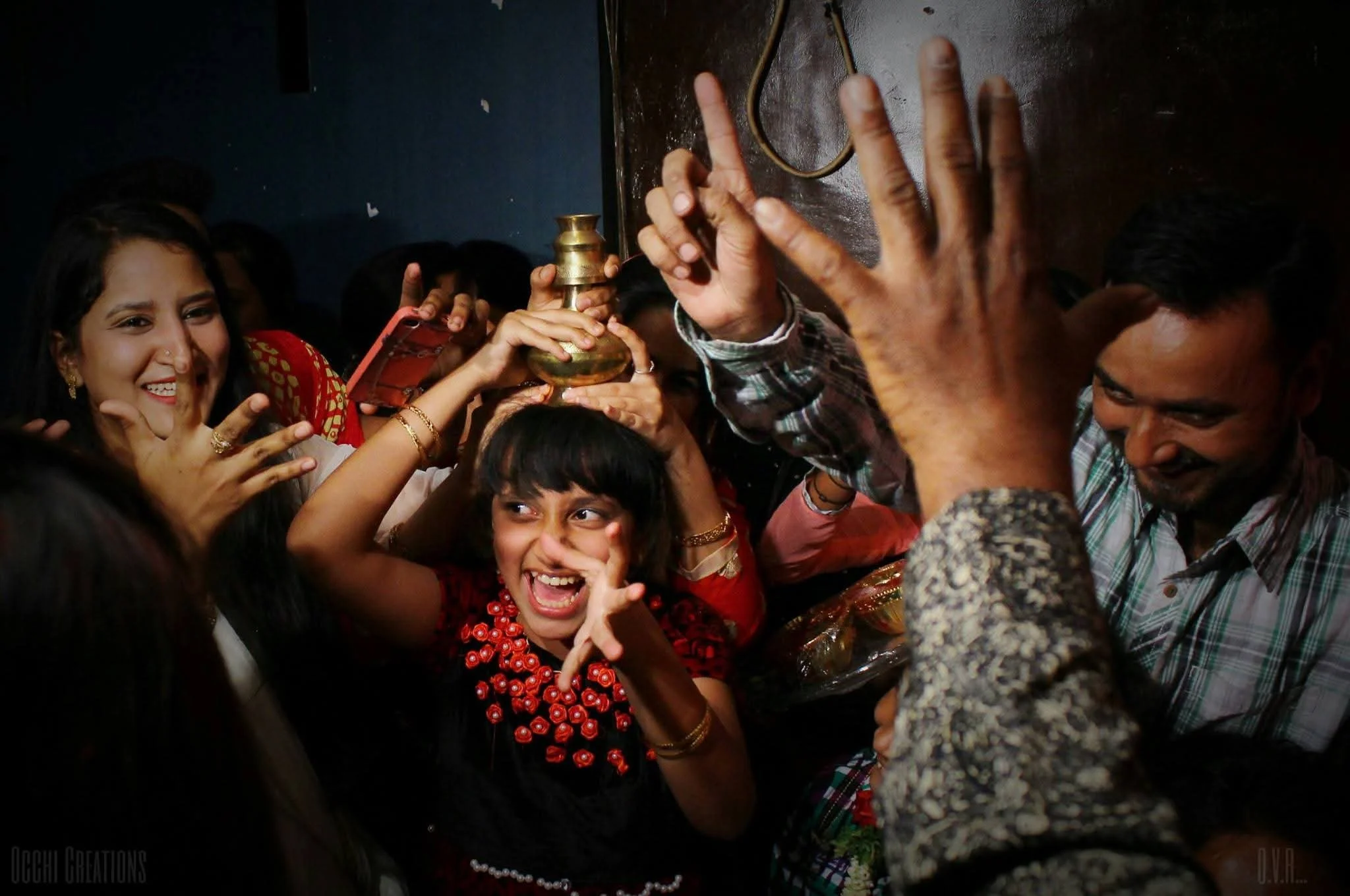 A group of people celebrating and laughing, with some holding a brass object, in a crowded indoor setting.