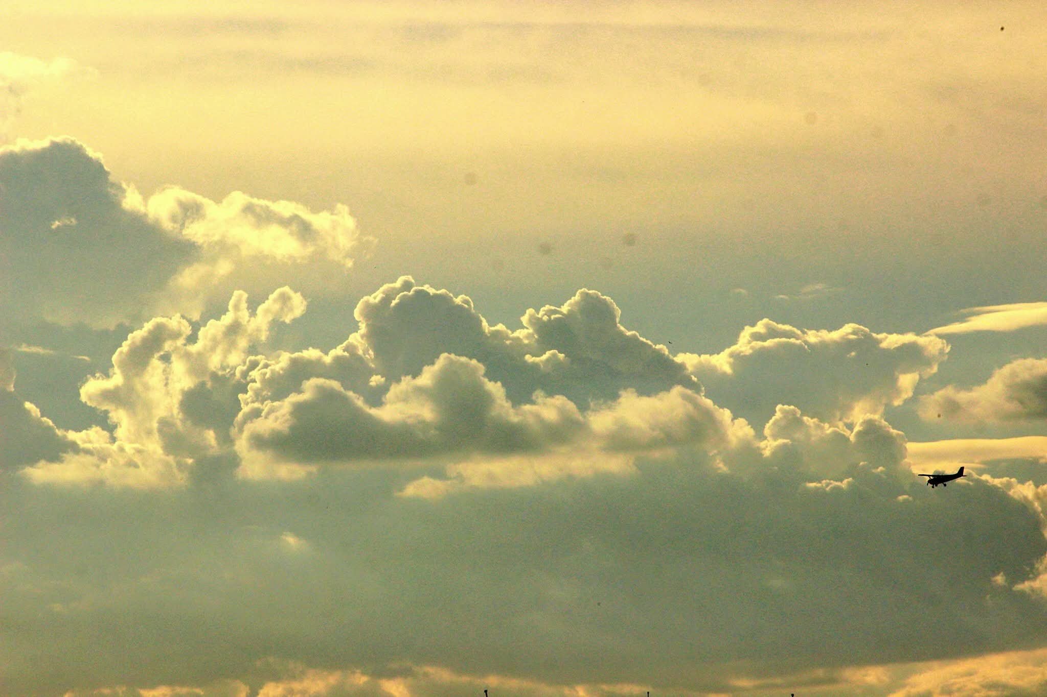 A sky filled with fluffy clouds and an airplane flying in the distance.