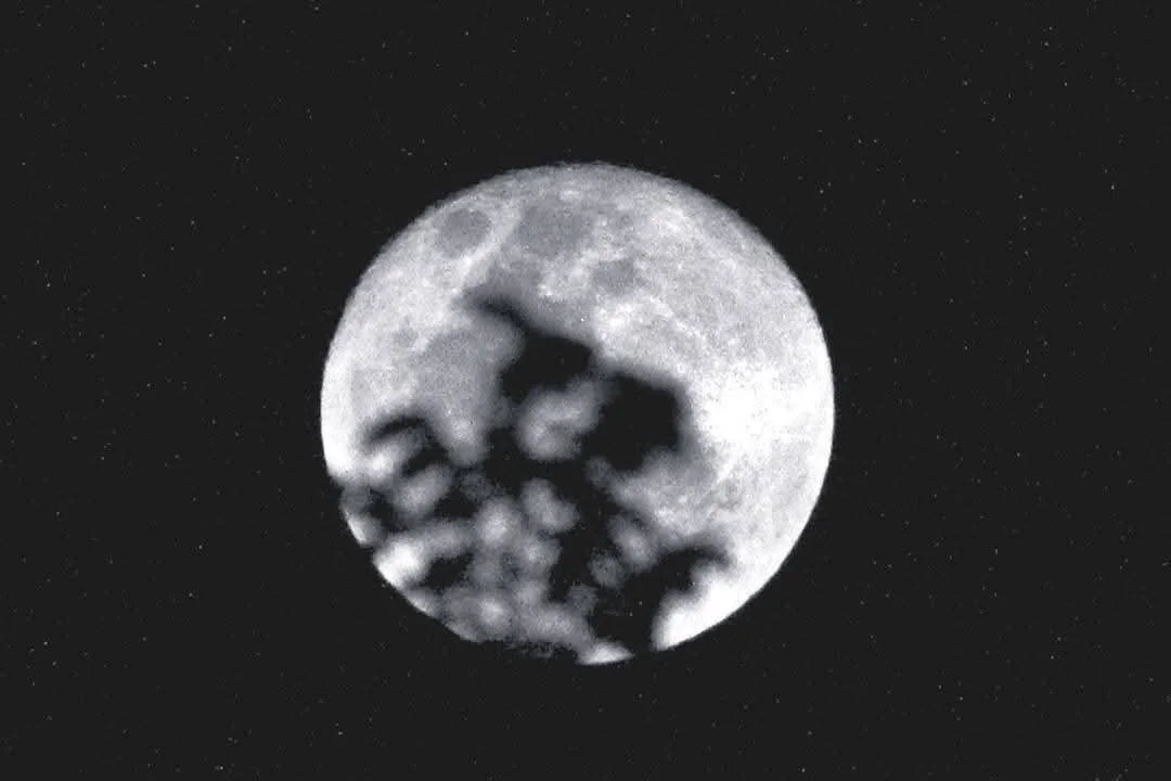 Close-up view of the moon with visible craters and clouds obscuring parts of its surface, set against a starry night sky.