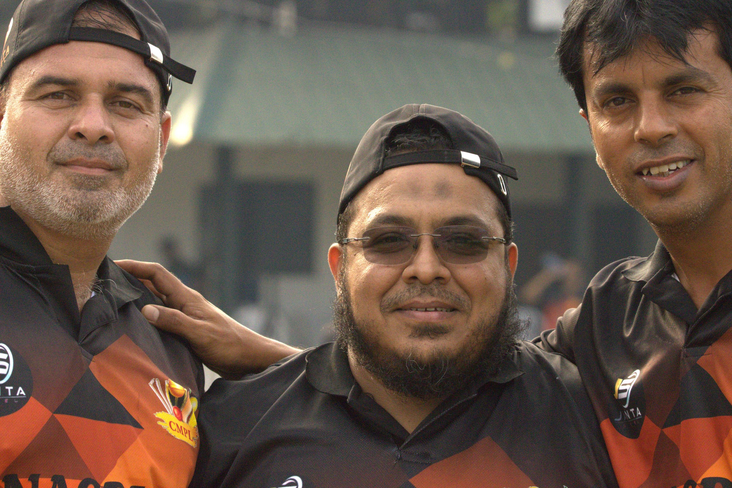 Three men in sports uniforms, standing close, smiling, with their arms around each other's shoulders, outdoors