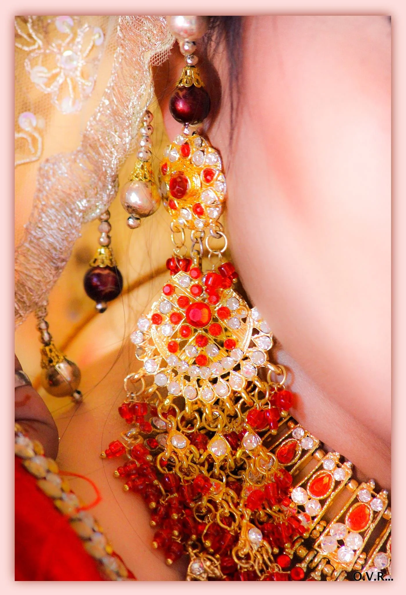 Close-up of an ornate gold and red jewelry set, including earrings, a necklace, and bangles, worn by a person dressed in traditional attire.