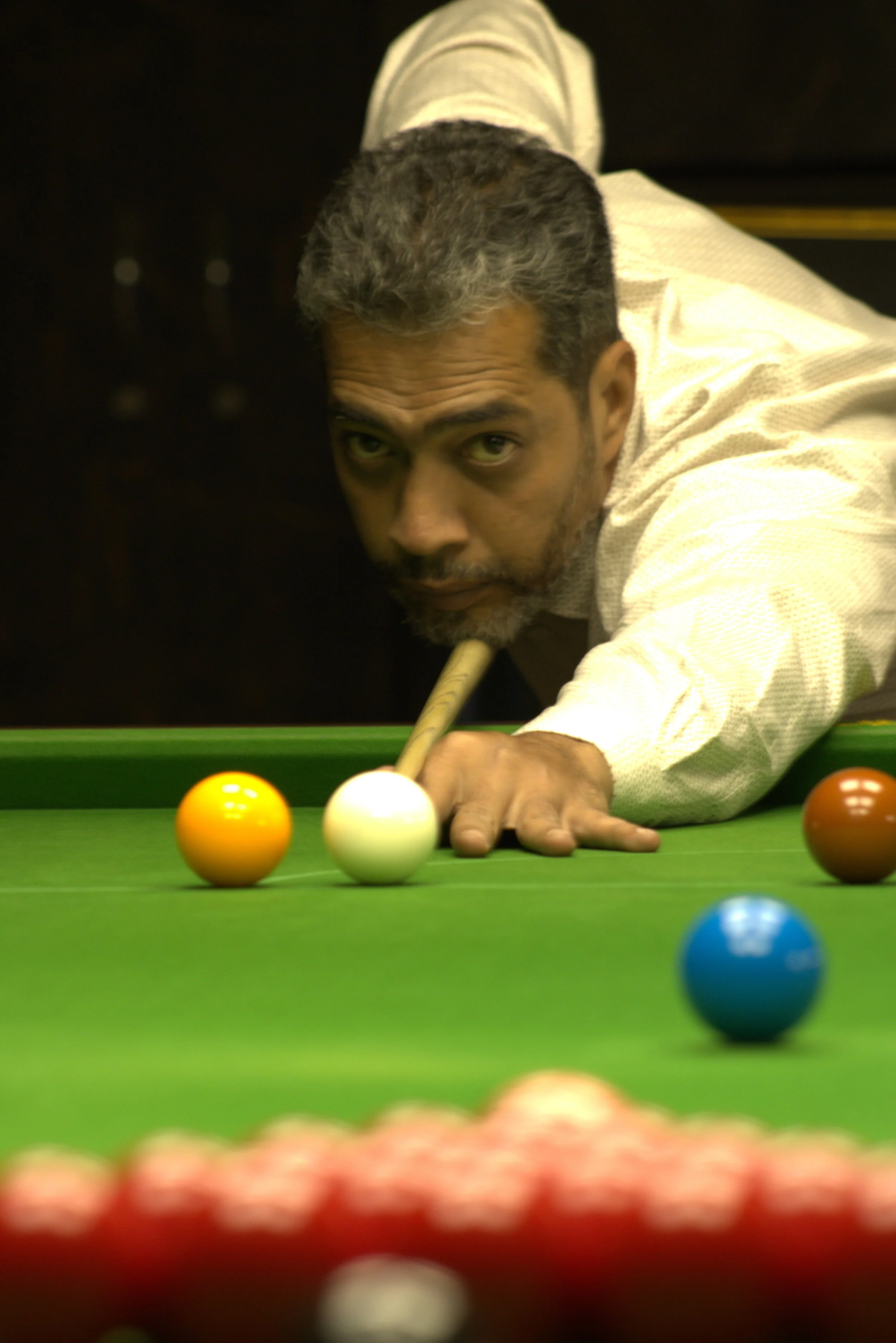 A man playing billiards, aiming with a cue stick at the white cue ball on a green pool table, surrounded by colored balls.