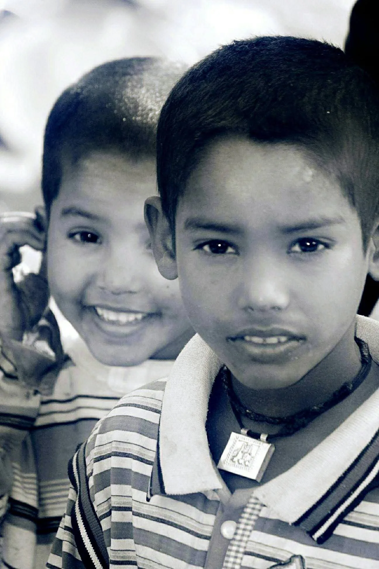 Two young boys with short hair, one smiling and the other with a serious expression, standing close together in a black-and-white photo.