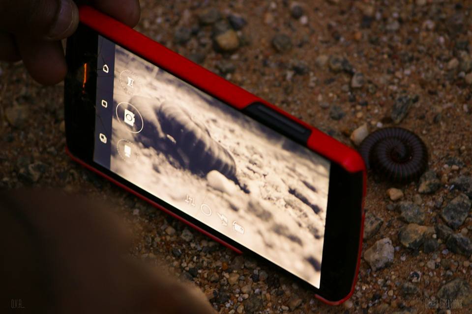 Smartphone on rocky ground taking a photo of a cloud formation that resembles a tornado or funnel cloud, with a small ammonite fossil nearby.