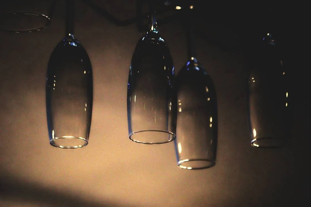Four upside-down wine glasses hanging from the ceiling in a dimly lit room.
