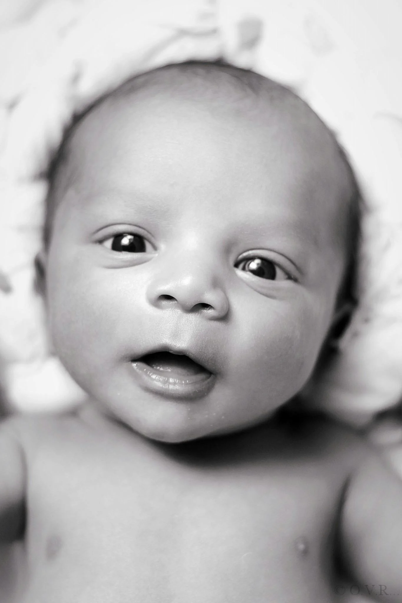 Black and white close-up photo of a baby's face with wide eyes and open mouth.