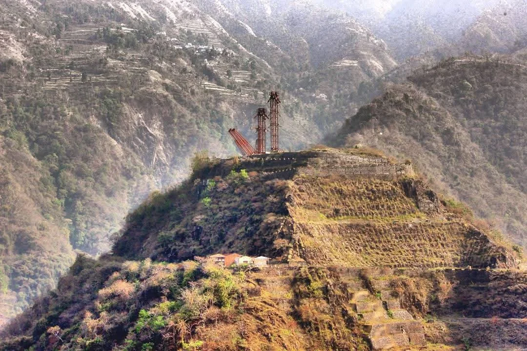 Ancient hillside terraces on a mountain with a weathered structure and old machinery on top.