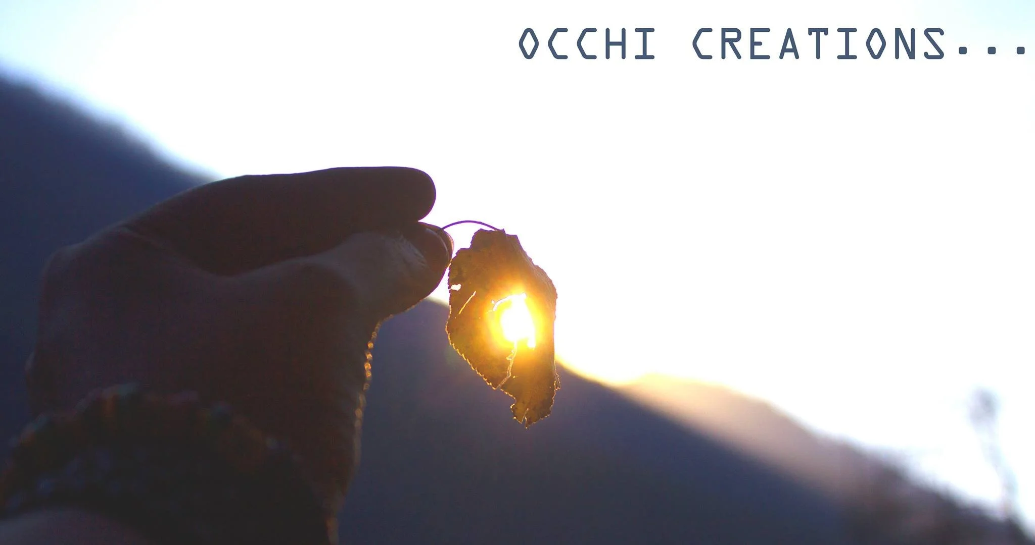 A hand holding a dried leaf against the sun with mountains in the background and text 'OCHI CREATIONS...' in the upper right corner.