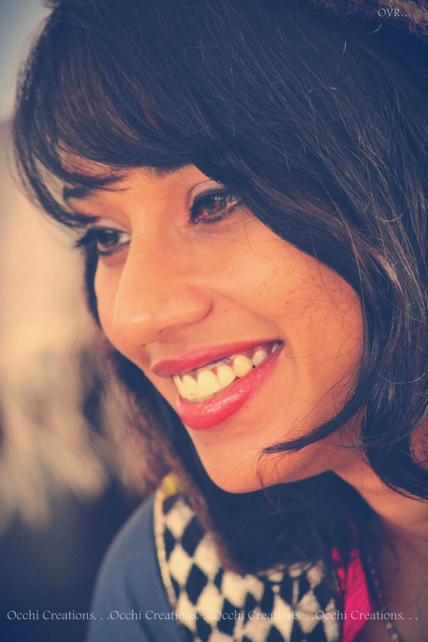 Close-up photo of a smiling woman with dark hair and makeup, showing her face and part of her upper body.