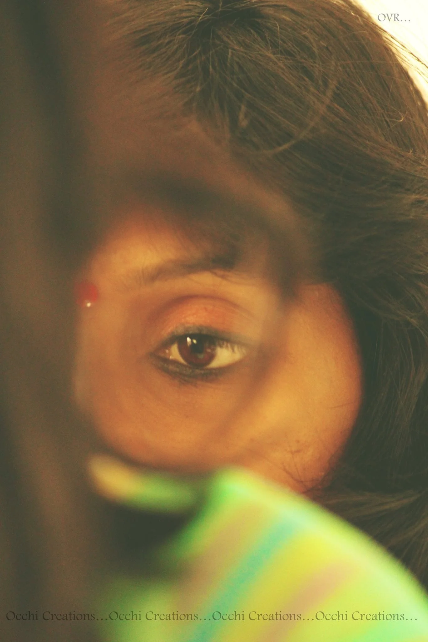 Close-up of a woman's face, partially obscured, with focus on her right eye, dark hair, and a hint of colorful clothing.