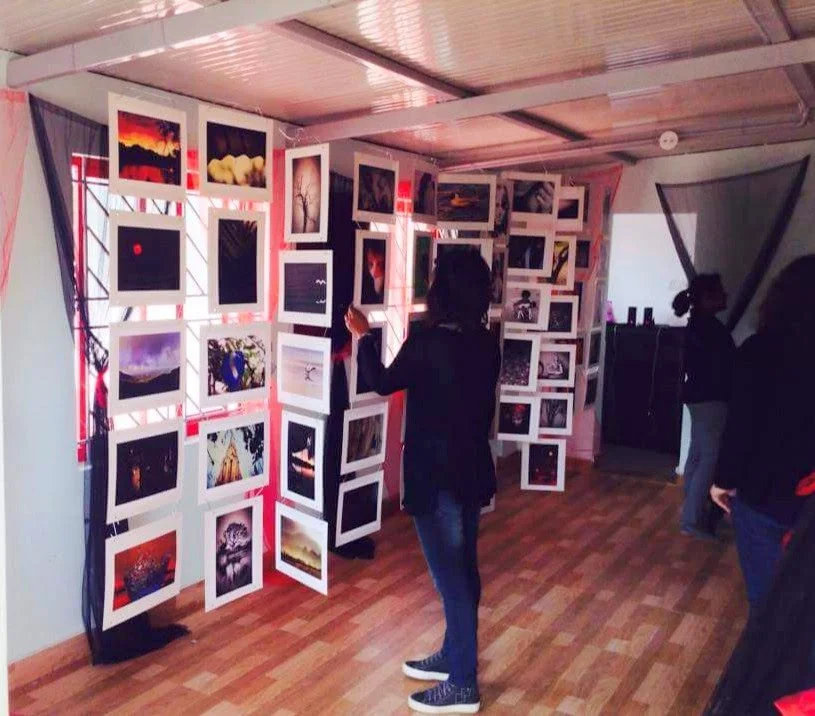 People viewing framed photographs or artwork displayed on a wall in an art gallery or exhibition space.