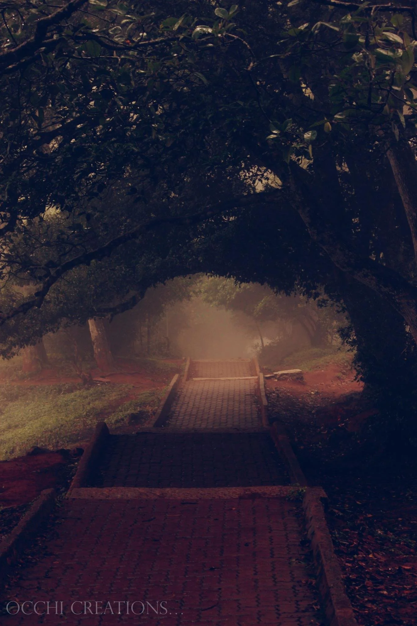 A winding brick pathway through a wooded park with trees arching overhead, mist in the distance, and soft lighting creating a calming atmosphere.