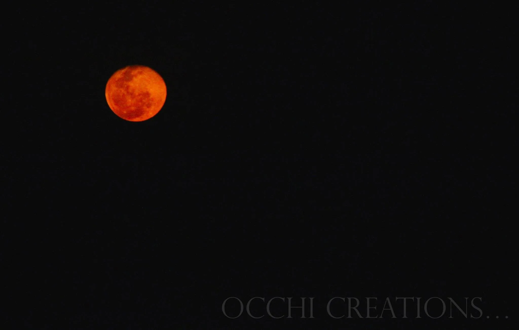A reddish-orange lunar eclipse moon against a black night sky.