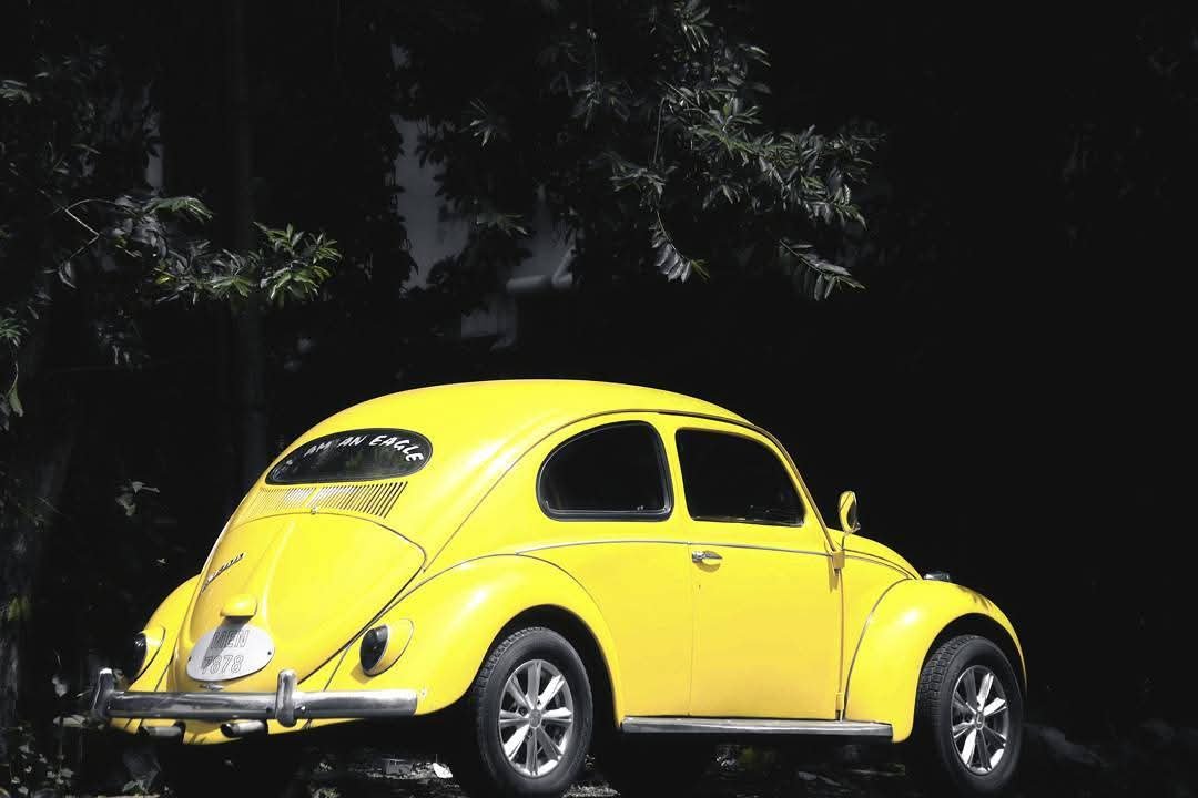 Bright yellow vintage Volkswagen Beetle car parked outdoors at night near trees.